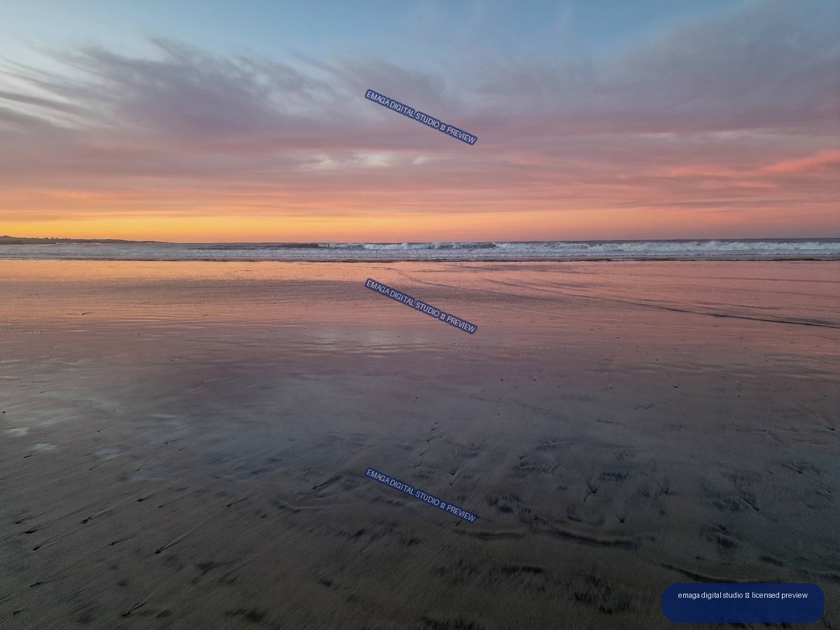 Pastel sunset over ocean waves at Famara Beach, reflected across broad wet sand.