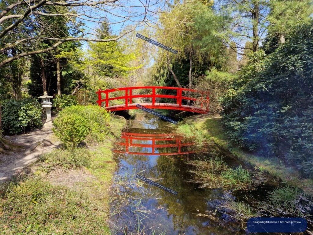 Red arched footbridge over a reflective garden stream