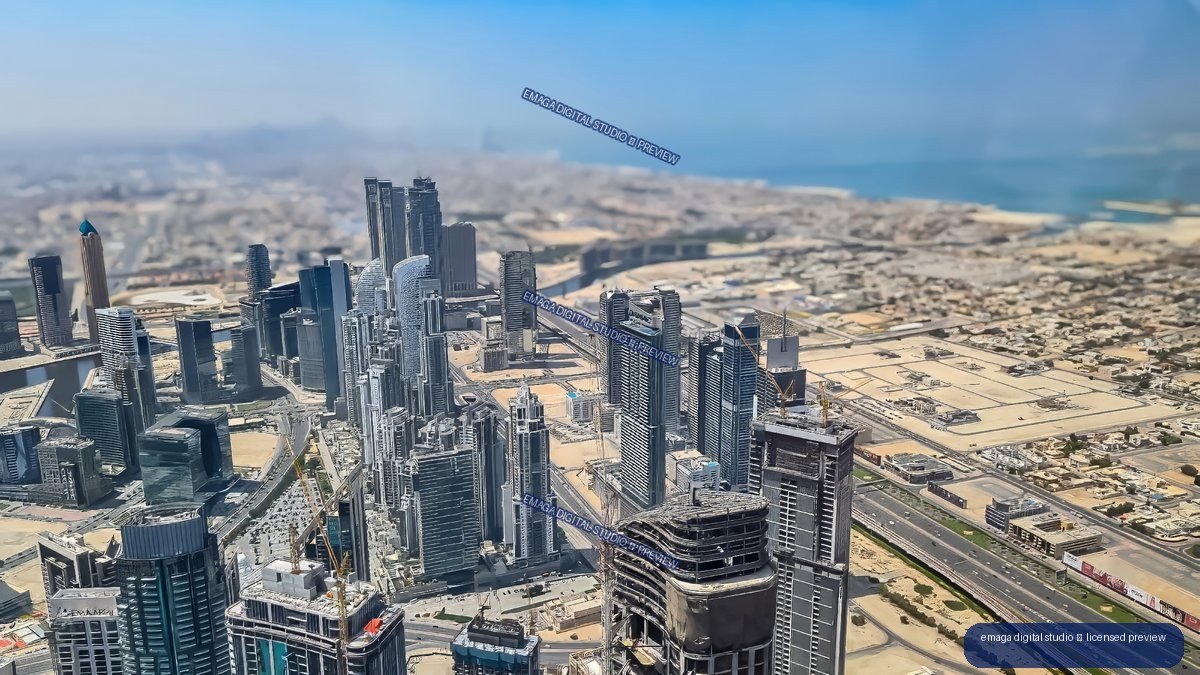 Aerial view of Dubai skyscrapers, roads, sandy development areas, and the Arabian Gulf beyond.