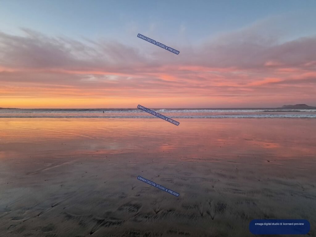 Pastel sunset over Famara Beach, with waves and pink reflections on wet sand and a distant landform at right.