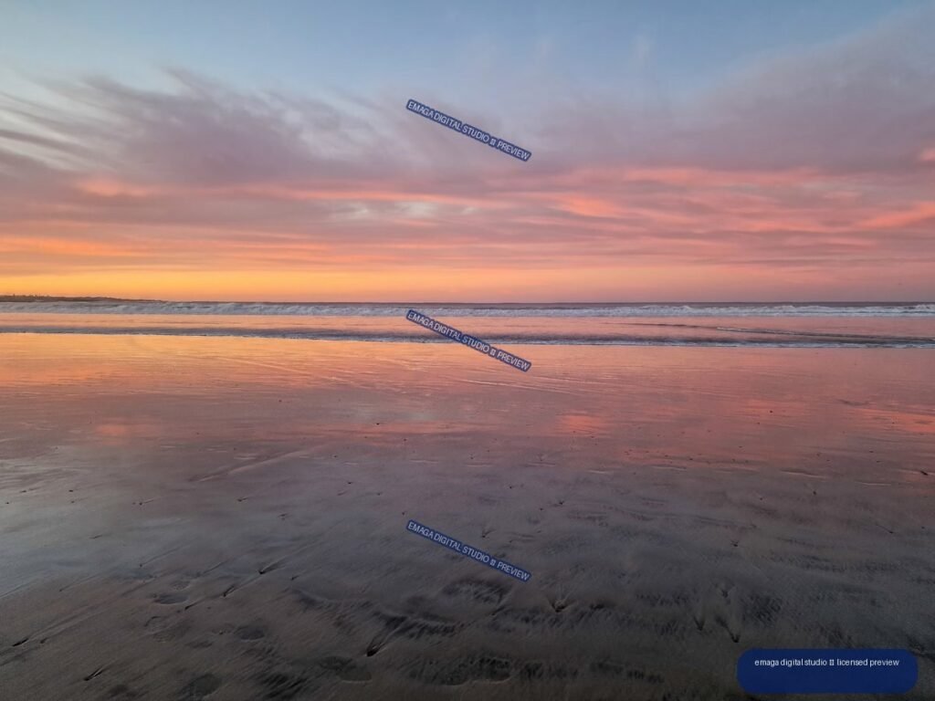 Pastel sunset over a beach, with waves and pink-orange reflections on wet sand.