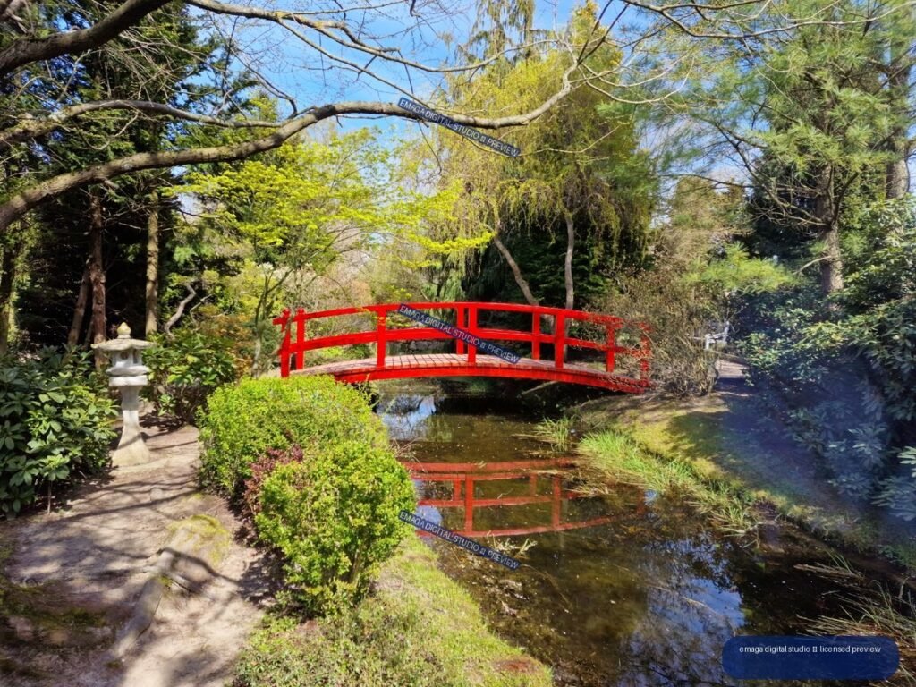Red arched footbridge over a pond in a landscaped garden — Hortulus Gardens, Dobrzyca