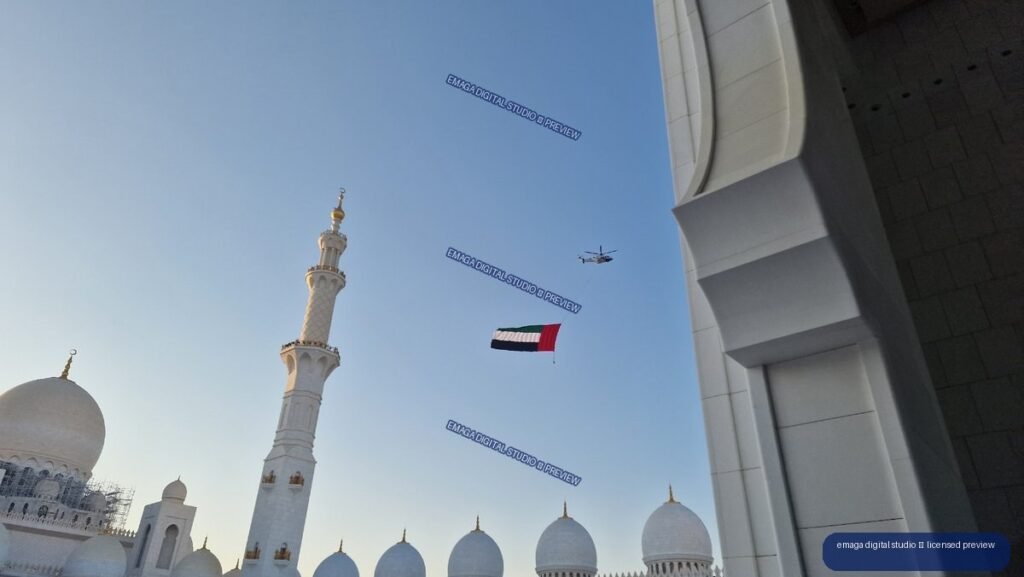 White mosque domes and minaret beneath a UAE flag and helicopter — Sheikh Zayed Grand Mosque, Abu Dhabi