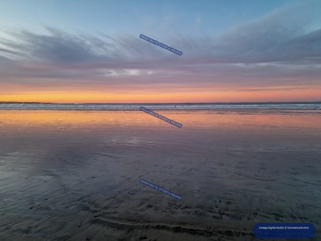 Sunset over a broad beach, with colorful sky and waves reflected in wet sand.