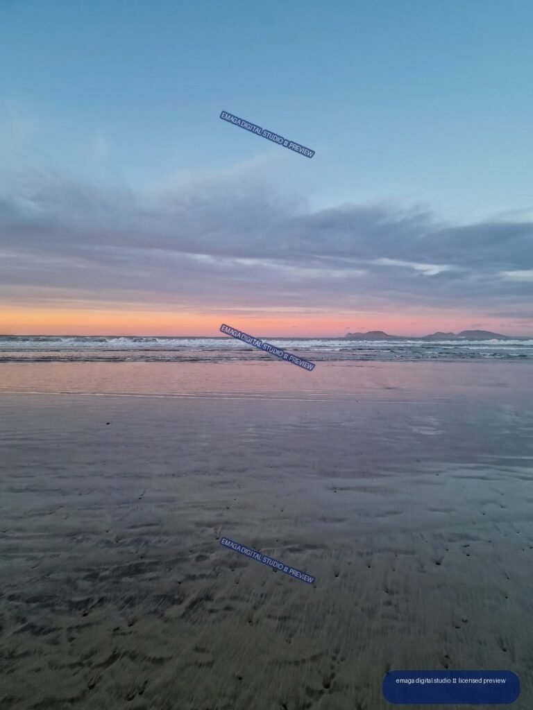 Wet reflective beach at dusk with gentle waves, layered clouds, and distant island silhouettes on the horizon.