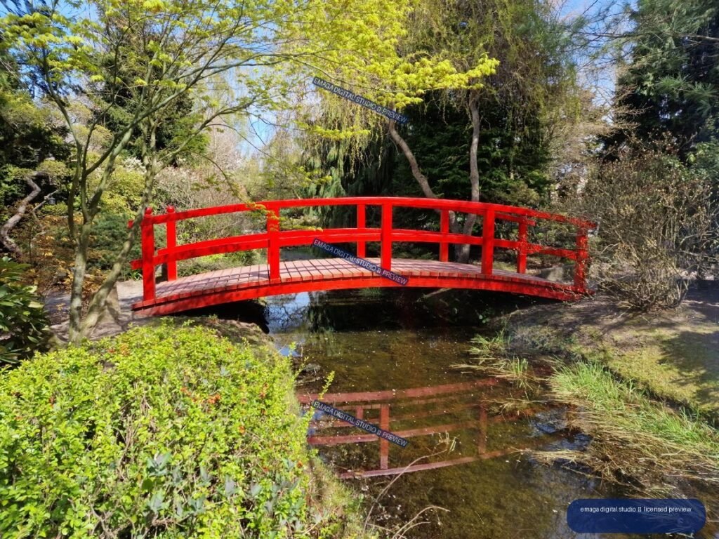 Red arched footbridge over a reflective garden pond