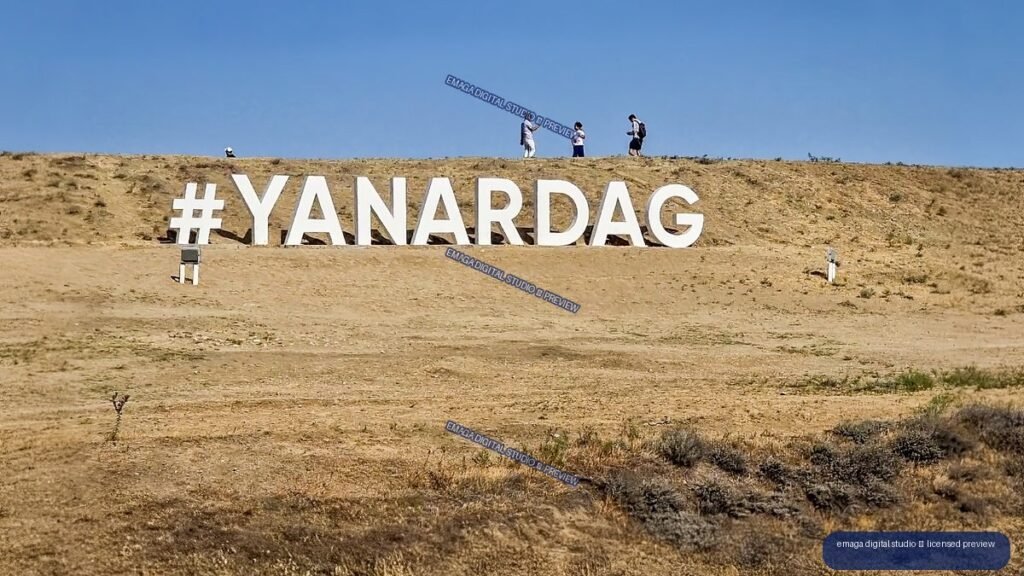 Large white #YANARDAG sign on a dry hillside beneath a clear blue sky, with visitors on the ridge.